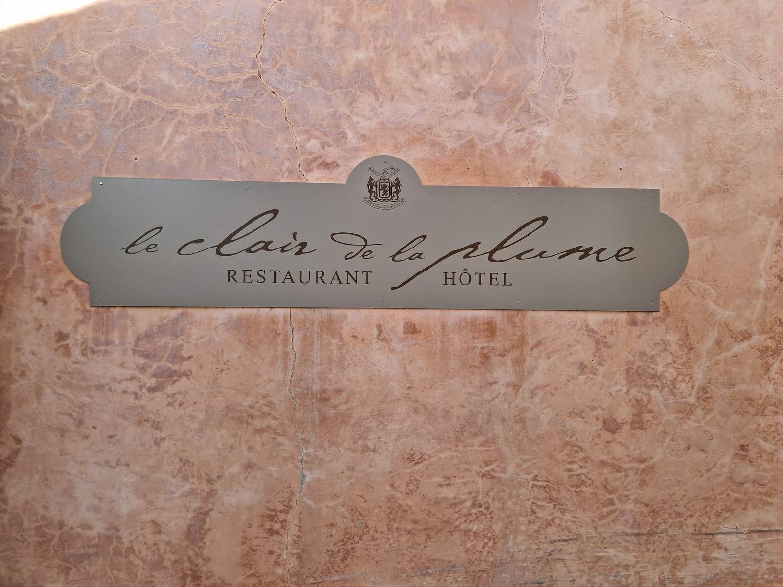 L'enseigne en métal du Clair de la Plume, restaurant et hôtel, sur un mur ocre