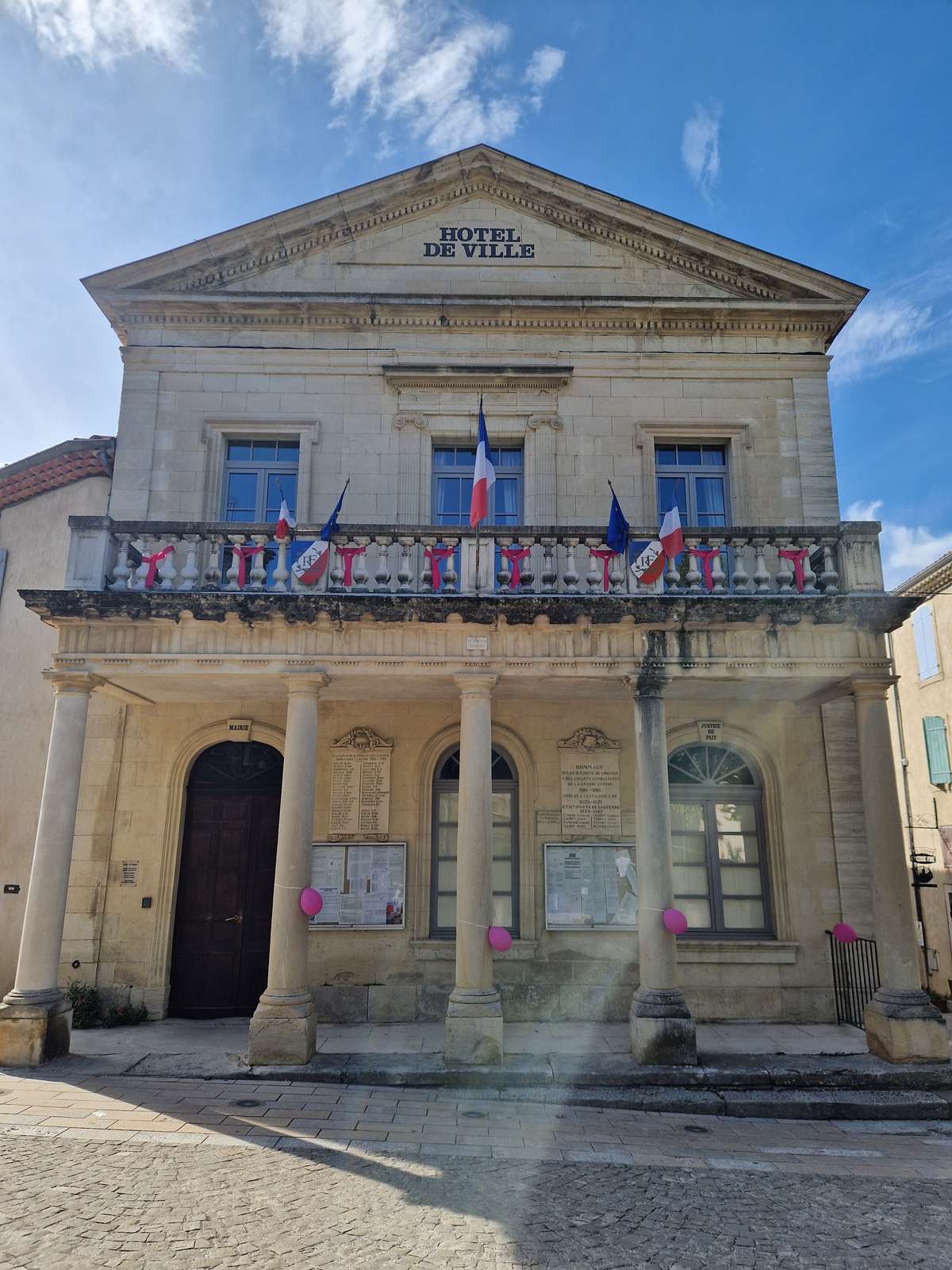 La façade néoclassique de la mairie de Grignan, avec ses colonnes, son balcon et ses drapeaux