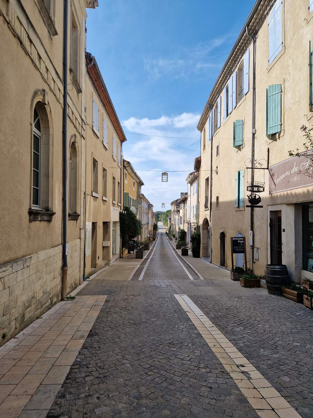Une rue piétonne de Grignan bordée de façades claires, avec quelques terrasses